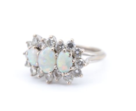 A 1970s diamond and opal dress ring, the central 6 x 5 mm opal line set between two smaller opals, their outline traced by 16