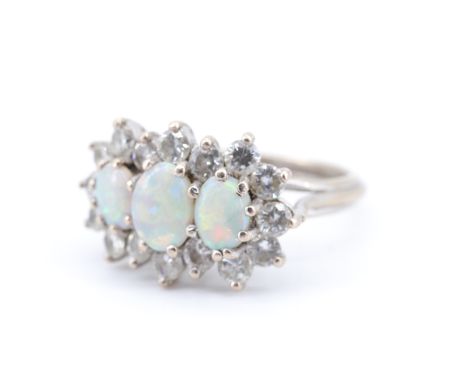 A 1970s diamond and opal dress ring, the central 6 x 5 mm opal line set between two smaller opals, their outline traced by 16