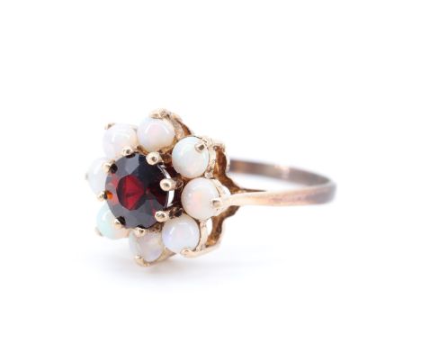 A late 20th Century lady's daisy set almandine and opal ring, the central 6 mm brilliant garnet above and surrounded by eight