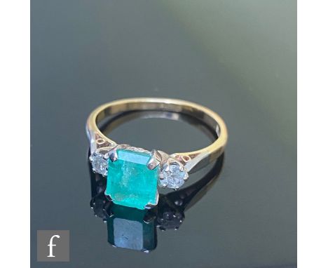 An 18ct emerald and diamond three stone ring, central emerald cut emerald, length 8mm, claw set and flanked by a single brill