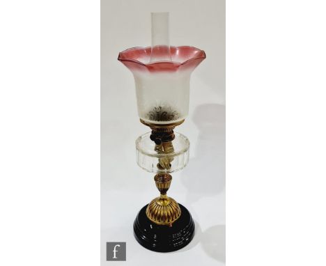 A Victorian brass oil lamp with part acid etched cranberry shade on a black glazed base, height 62cm. 