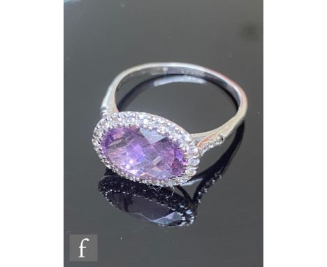 A 9ct amethyst and diamond cluster ring, central faceted cut oval amethyst within a twenty stone diamond surround and diamond