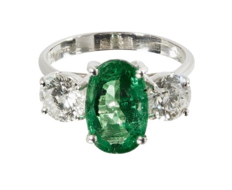 An emerald and diamond set three stone ringclaw set with an oval cut emerald, flanked to either side by a single round brilli