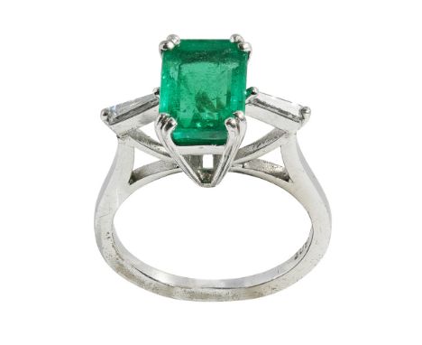 An emerald and diamond set ringclaw set with a trap cut emerald, each shoulder set with a tapering baguette cut diamond, to a