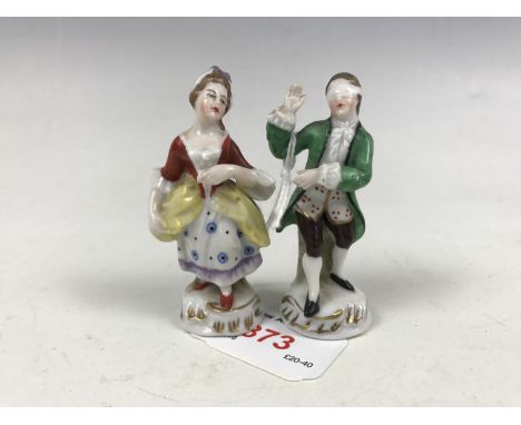 A pair of late 19th / early 20th Century porcelain figurines, depicting a maiden in 18th Century dress and a blindfolded gent