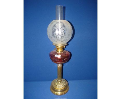 A Cranberry glass oil lamp having brass reeded column and floral shade.
