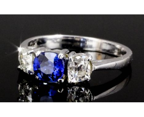 A modern silvery coloured metal mounted sapphire and diamond set three stone ring, the central circular cut sapphire approxim