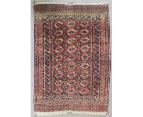 An antique Saryk Turkmen rug woven in navy blue, brown, pink and ivory with three rows each of nine guls on a madder ground w