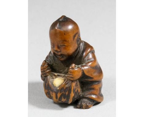 A Japanese boxwood netsuke, carved in the form of a seated boy opening fruit, 1.5ins (37mm) high, unsigned