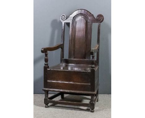 A late 17th/early 18th Century oak armchair, the arched panelled back with scroll carved cresting, box seat, on bobbin turned