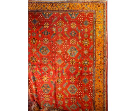 A Turkey carpet woven in colours with a stylised floral design on a terracotta ground within conforming three stripe borders,