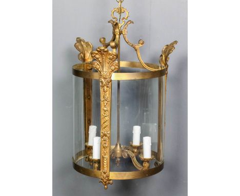 A lacquered brass and glass cylindrical four light hall lantern on scroll supports, the uprights cast with leaf, bellflower a