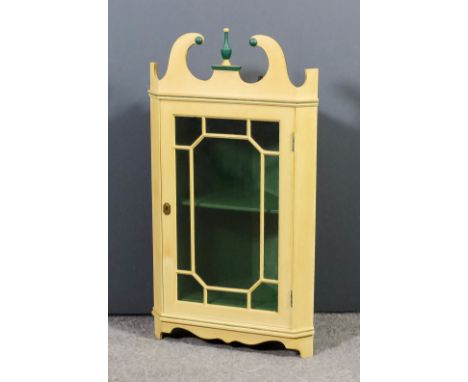 A cream and green painted hanging corner cupboard of Georgian design, with swan neck pediment, fitted one shelf enclosed by a