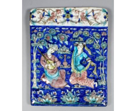 A 19th Century Qajar rectangular tile with moulded and painted decoration of two figures in a garden, one a man playing a str