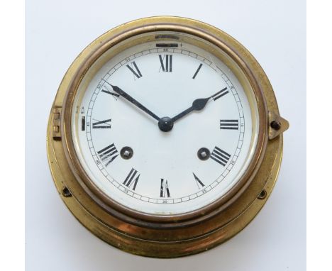 A brass cased bulkhead clock, with an enamel dial featuring Roman Numerals, an eight day movement, and a diameter of 18cm.Con