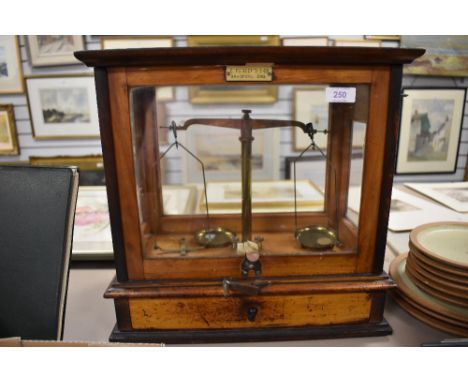 An antique cased set of apothecary or chemist balance scales in a glazed cabinet.