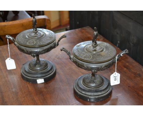 A pair of 19th century dark patinated bronze saucer shaped pedestal mantel urns and covers, stork finials, cast in relief wit