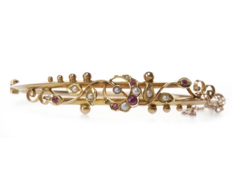 EDWARDIAN NINE CARAT GOLD RUBY AND SEED PEARL BANGLEof oval form, with a central ruby and pearl set crescent motif with radia