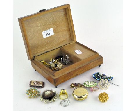 A wooden jewellery box, containing a selection of brooches, an enamel pill box, rings and more