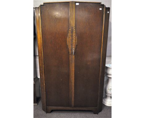 An Art Deco oak wardrobe with indented corners and carved fluted panel to the centre, with mirror, shelf and hanging rail to 