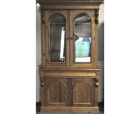 A tall pine dresser with carved acanthus brackets, three shelves behind glazed arched double doors, and two drawers of curved