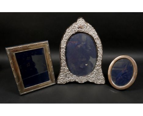Three ERII silver photograph frames, comprising an oval form frame, decorated with foliate and scroll repousse designs and a 