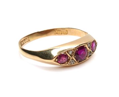 An 18ct yellow gold, three stone ruby and diamond ring, the central round cut ruby, 3.5 by 3.0mm, flanked by a smaller ruby, 