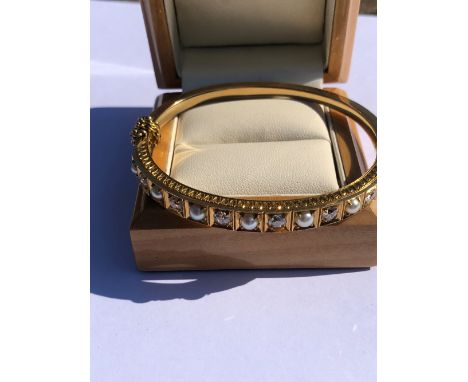 AN ANTIQUE DIAMOND AND PEARL GRADUATED HINGED BANGLE, COMPLETE WITH ADDED SAFETY CHAIN. UNHALLMARKED ASSESSED AS 14-15ct GOLD