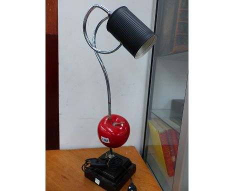 A NOVELTY TABLE LAMP, THE BLACK TIN CAN STYLE SHADE ON A COILED CHROME ARM PIERCING A RED APPLE ABOVE THE STEPPED SQUARE FOOT