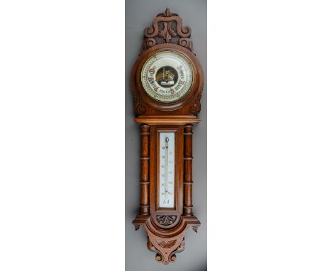A Victorian oak framed aneroid barometer, the carved case with pediment above column supports, the lower cream enamel dial wi