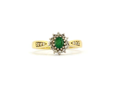 A hallmarked 18ct yellow gold cluster ring set with an oval cut emerald surrounded by diamonds and diamond set shoulders, (R 