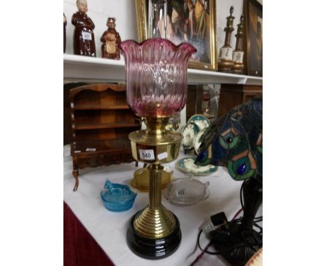 A brass oil lamp on black pottery base and with later cranberry glass shade