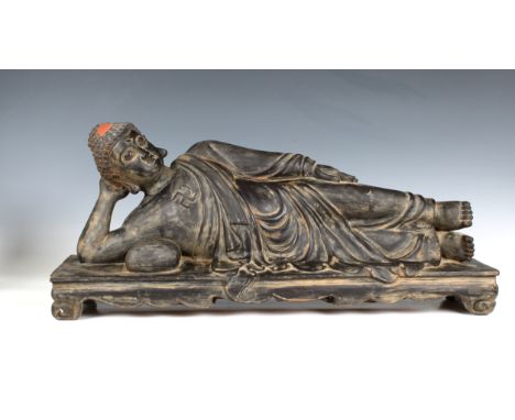 A carved and painted hardwood statue of the Buddha reclining on a day bed, with swastika motif on chest, 25½ inches long (65c