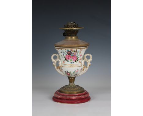 An antique ceramic urn shaped oil lamp decorated with floral sprays, twin foliate scroll handles, to circular base, brass bur