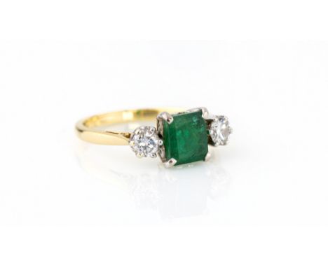 An 18ct yellow gold, emerald and diamond three stone ring the central 6.75 x 6mm. emerald flanked by two 0.20ct brilliant cut