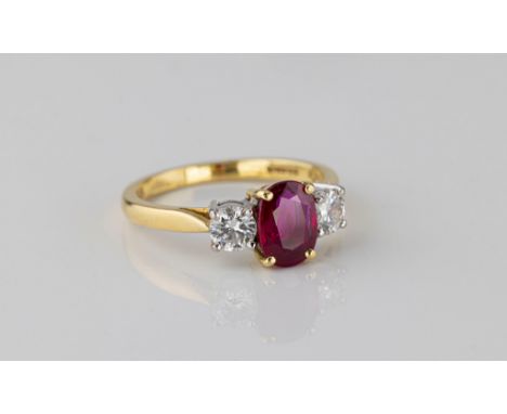 An 18ct yellow gold, ruby and diamond three stone ring the central, 8 x 6mm. oval cut, vivid purplish-red ruby with good clar