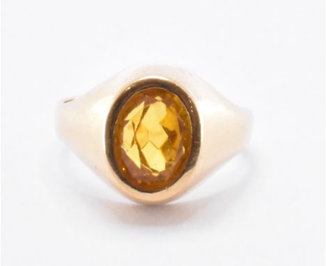 A gold signet ring being set with an oval cut orange paste stone. Marks to the interior of the band illegible, tests indicate