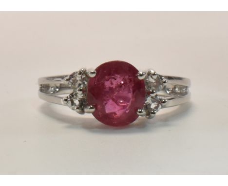 A hallmarked ruby and topaz ring. The ring set with a central oval cut ruby flanked by two sets of round cut topaz. Hallmarke