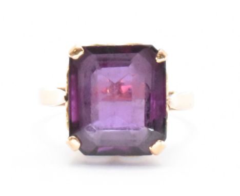 A gold and amethyst dress ring. The ring being set with a emerald cut amethyst in a basket setting on a plain band. Metal unm