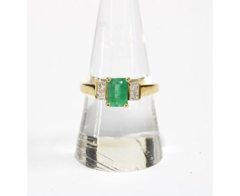 18ct gold emerald and diamond ring, the central emerald is in a four claw setting and flanked by two bright cut diamonds, sta