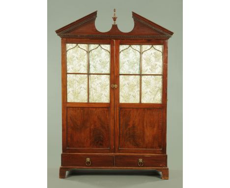 A George III wardrobe, with detachable broken arch pediment above a pair of glazed doors to open interior and raised on a bas