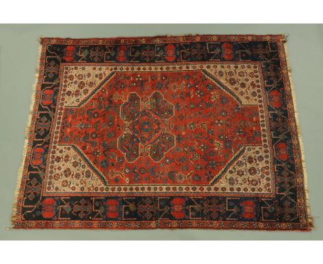 An Eastern fringed rug, principal colours red, black, blue and beige, the centre rectangular panel with corner spandrels flan