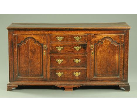 A Georgian oak dresser base, with a series of four central graduated drawers flanked by two panelled doors, all on short brac