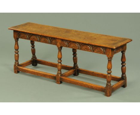 An oak stool, large rectangular form, with moulded edge, carved frieze and raised on six turned legs united by stretchers.  L
