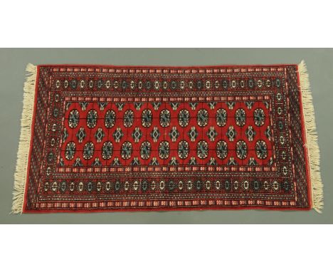 An Indian Bokhara fringed rug, with centre rectangular panel and multiple line border, principal colours red, black and green