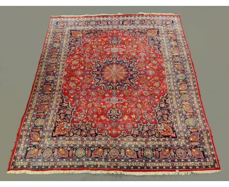 A large Iranian carpet, with fringed ends and repeating foliate pattern, principle colours red, blue and beige. 284 cm x 382 