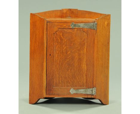 An early 20th century oak Arts &amp; Crafts hanging corner cupboard, with single door with stylised hinges opening to a shelf