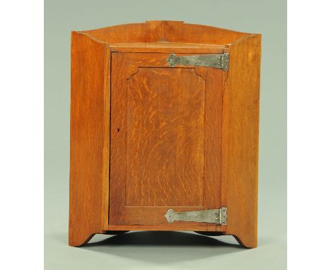 An early 20th century oak Arts &amp; Crafts hanging corner cupboard, with single door with stylised hinges opening to a shelf