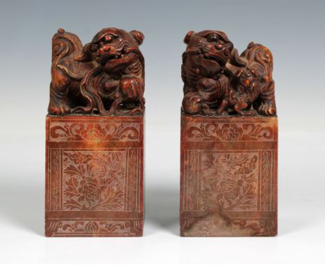 A pair of Chinese carved soapstone scroll weights, Surmounted with Dogs of Fo, the bases carved with scrolling foliate design