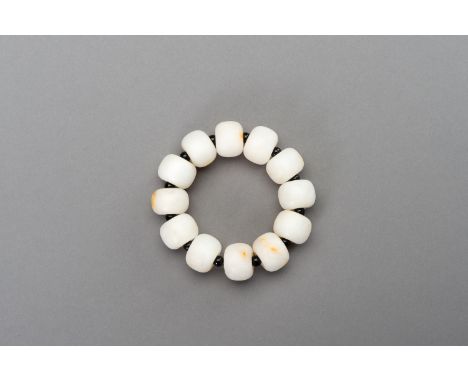 A WHITE AND RUSSET JADE BRACELET, 20th CENTURYChina. Comprising of twelve jade beads, spaced by smaller black beads, strung o